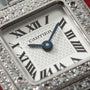 Cartier watch face with Roman numerals and blue hands, surrounded by diamond-set bezel on metal case.