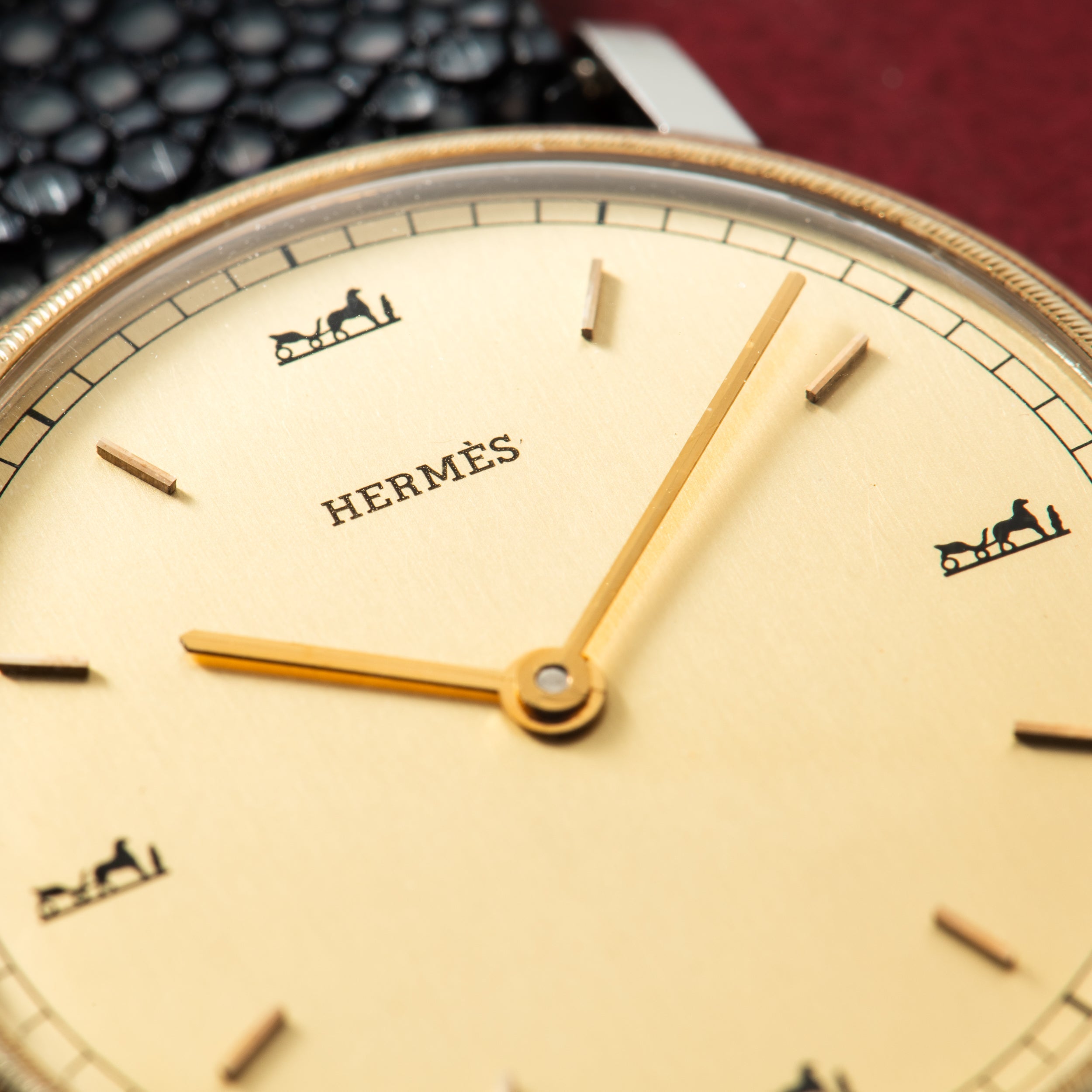 Hermès watch with cream dial, gold hands, hour markers, and carriage logo at 12 and 6 o'clock positions.