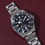 Stainless steel dive watch with black dial, white hour markers, rotating bezel, and metal bracelet on burgundy background.