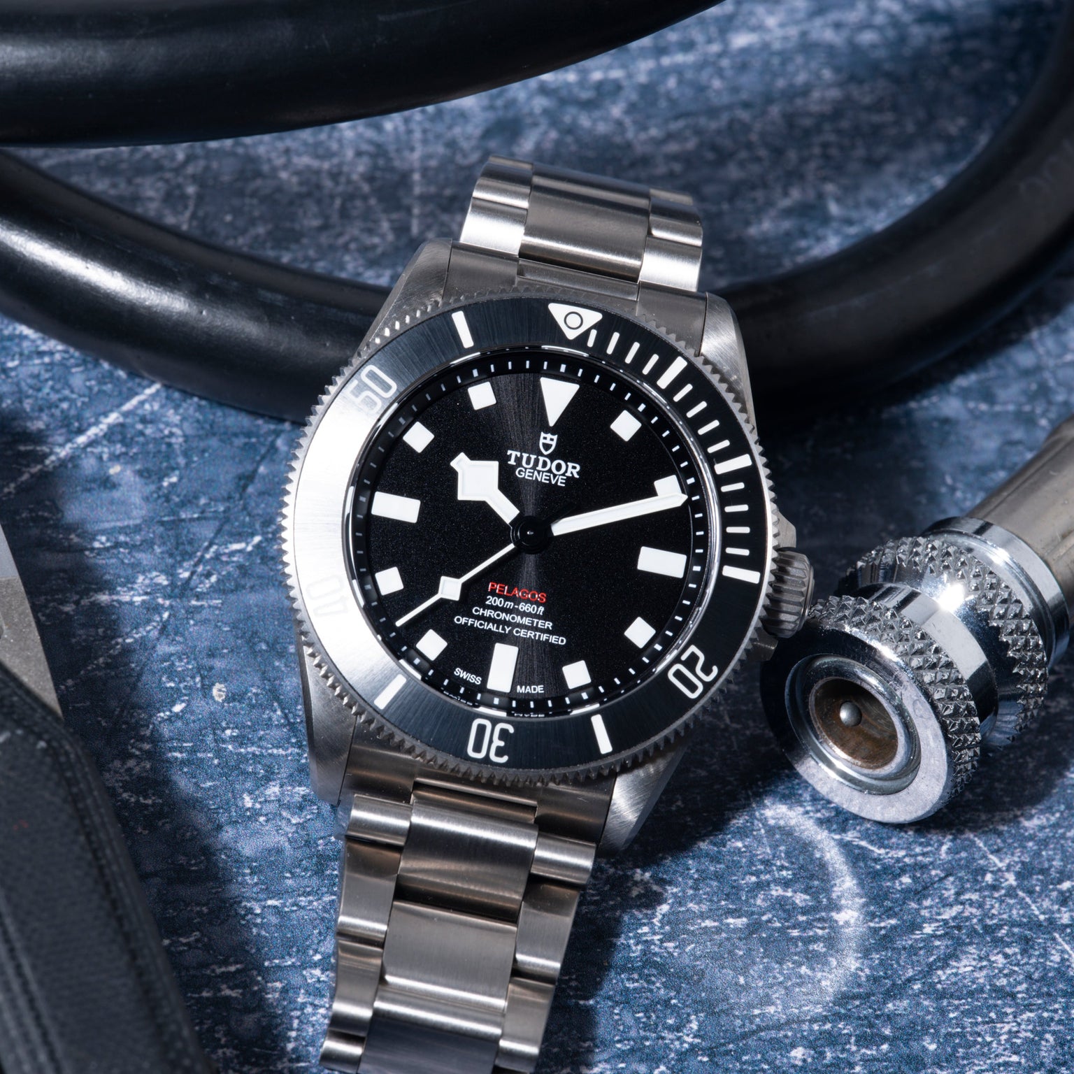 Tudor Pelagos 39 dive watch with stainless steel bracelet and black dial on blue textured surface with diving equipment.