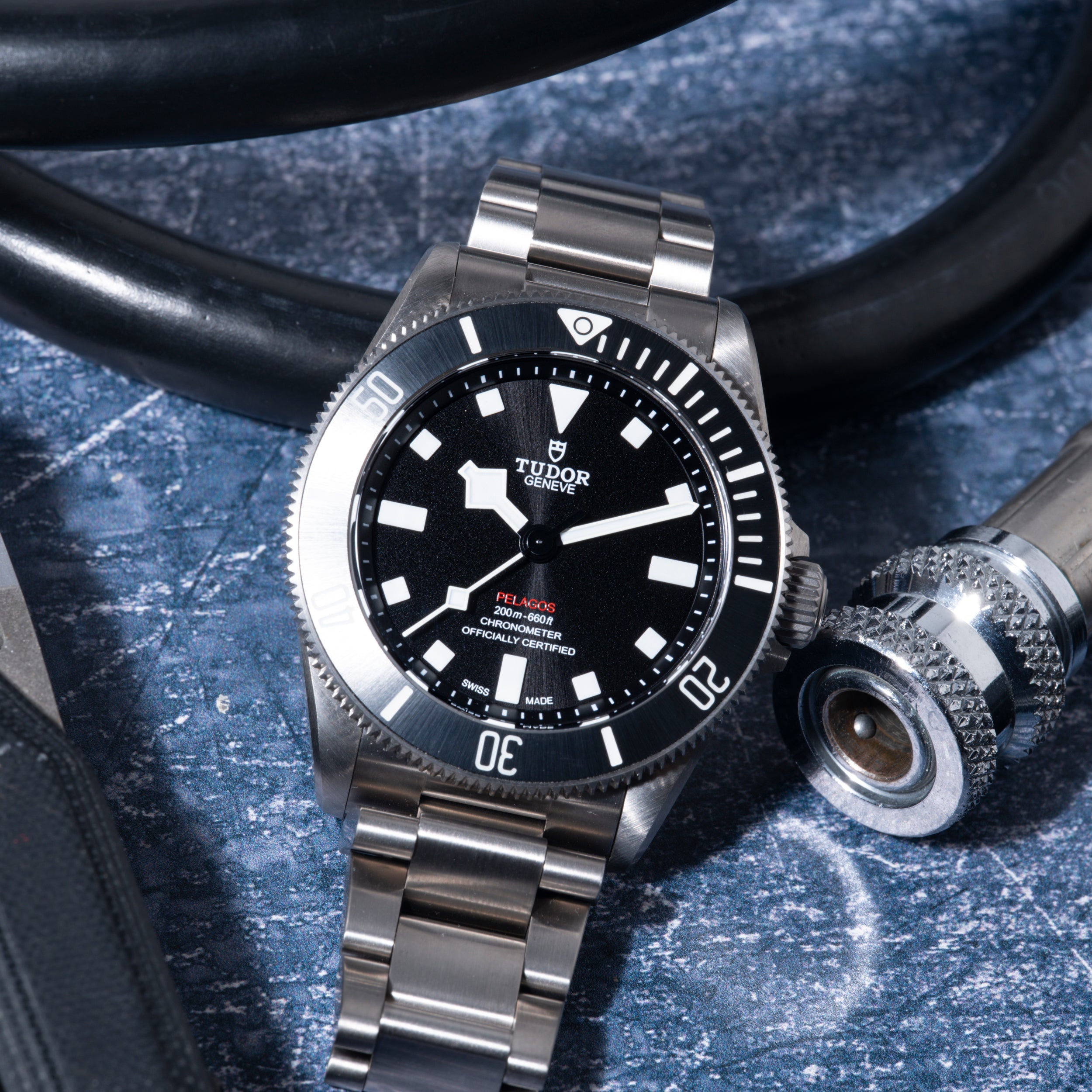 Tudor Pelagos 39 dive watch with stainless steel bracelet and black dial on blue textured surface with diving equipment.