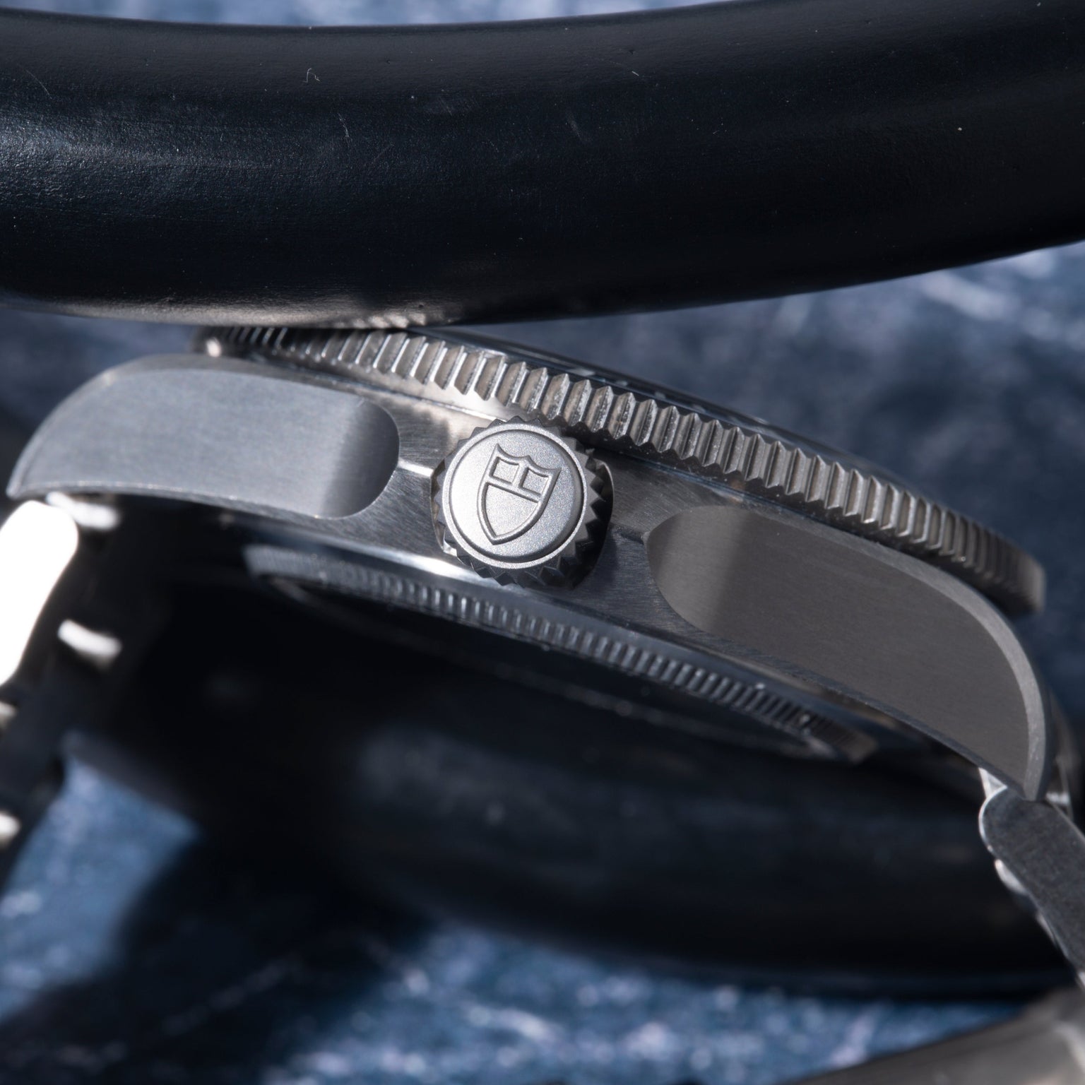 Close-up of Tudor Pelagos 39 watch case showing black bezel, metal crown with shield logo, and blue fabric strap.