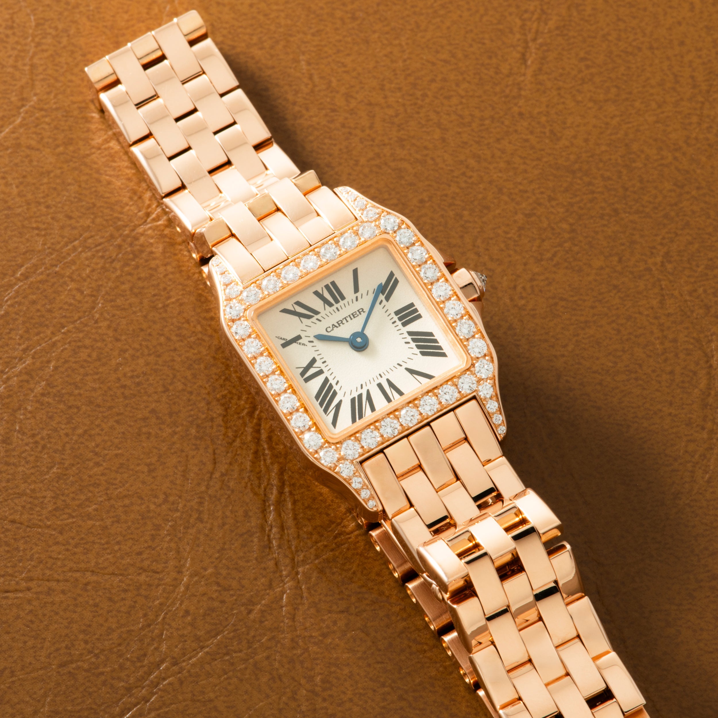 Rose gold square watch with diamond-set bezel, cream dial, Roman numerals, and matching link bracelet on tan leather backgrou