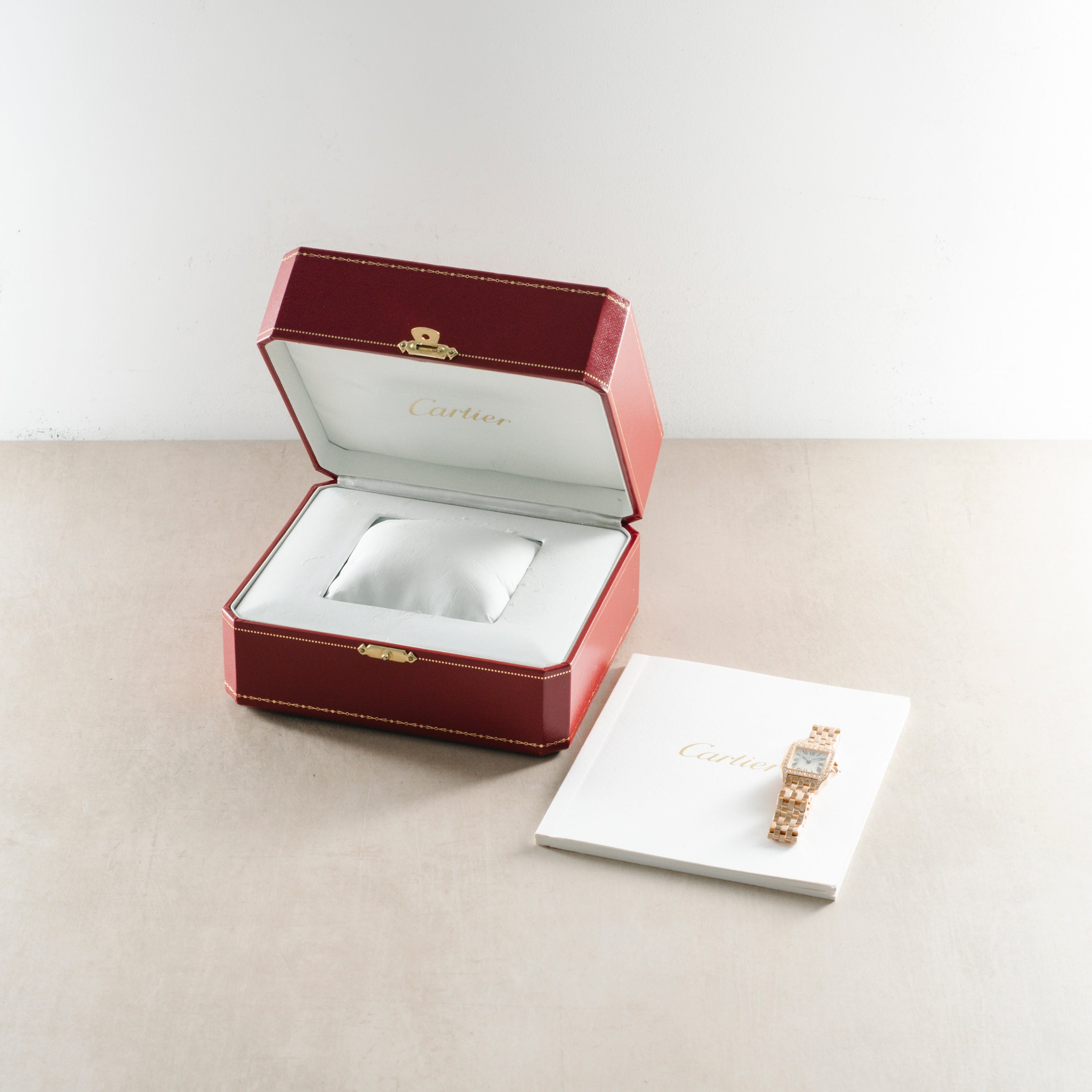 Rose gold rectangular wristwatch with diamond bezel displayed in burgundy Cartier box and on white card.