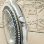 Silver watch with black bezel and textured dial, shown from side angle on a map background.