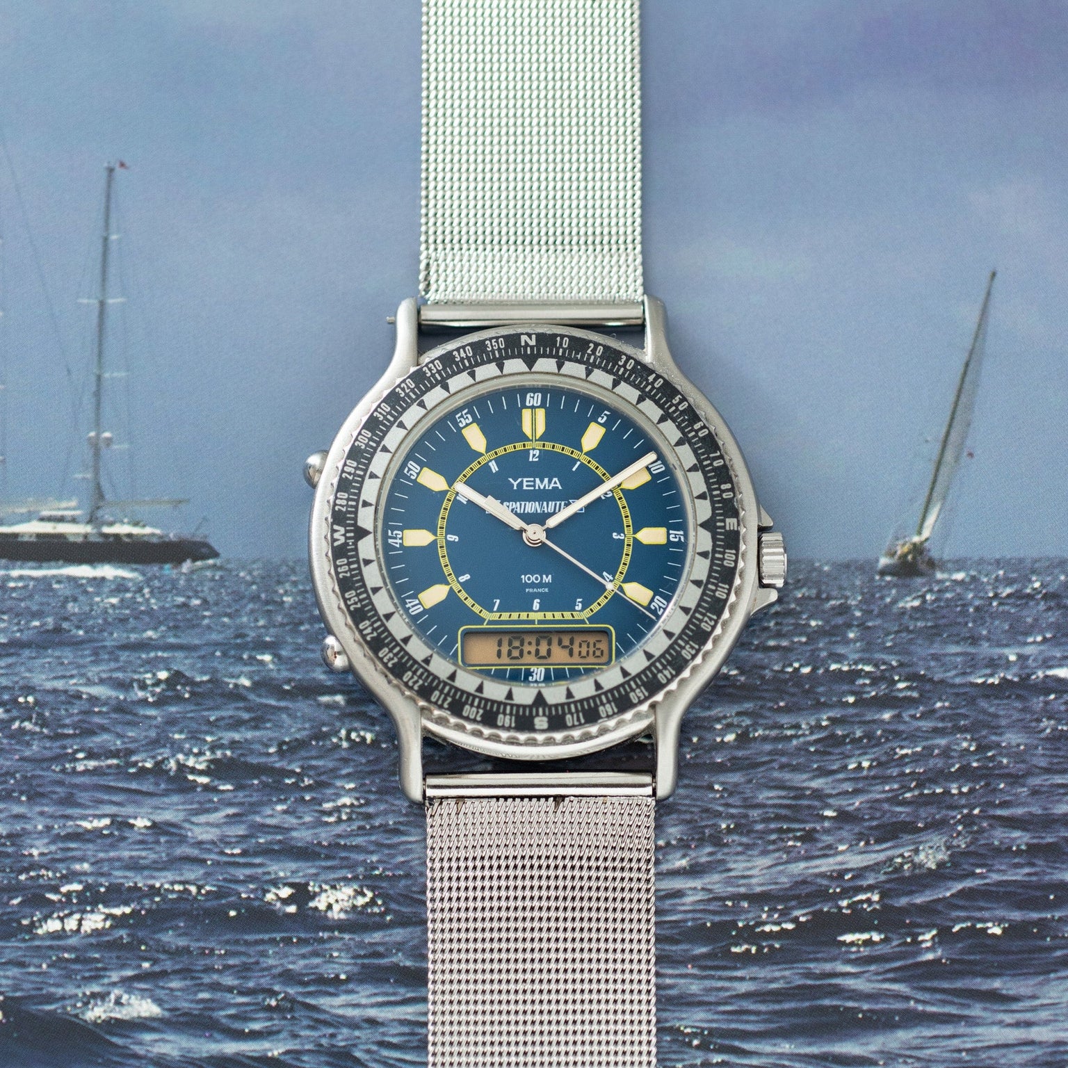 Yema Spationaute ISS watch with blue dial, yellow accents, digital display, stainless steel mesh band, and rotating bezel.