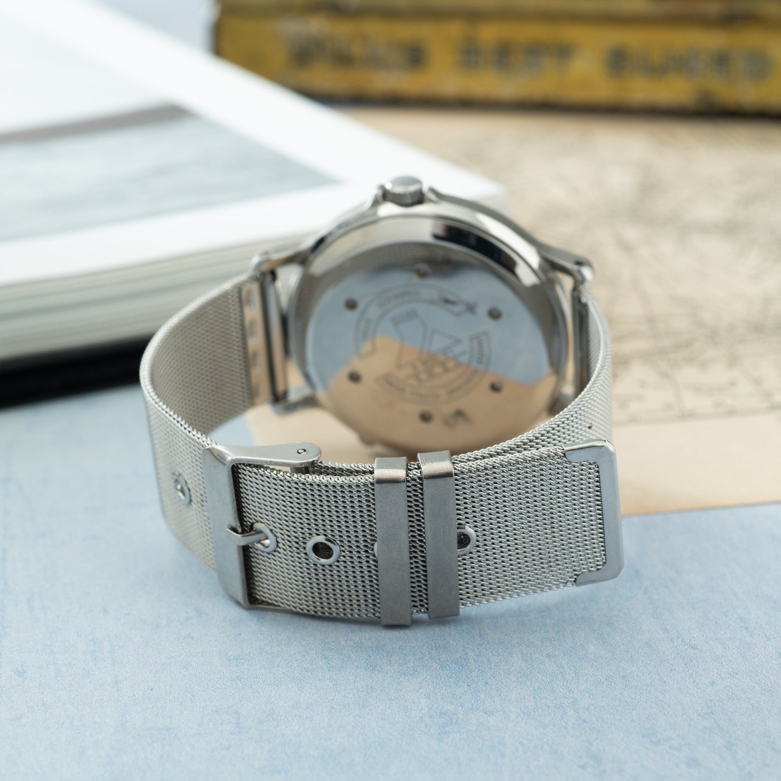 Silver-tone watch with mesh band and light blue dial featuring orbital design details, displayed caseback-up.