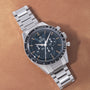 Stainless steel chronograph watch with black dial, orange accents, tachymetre bezel, and three subdials on metal bracelet.