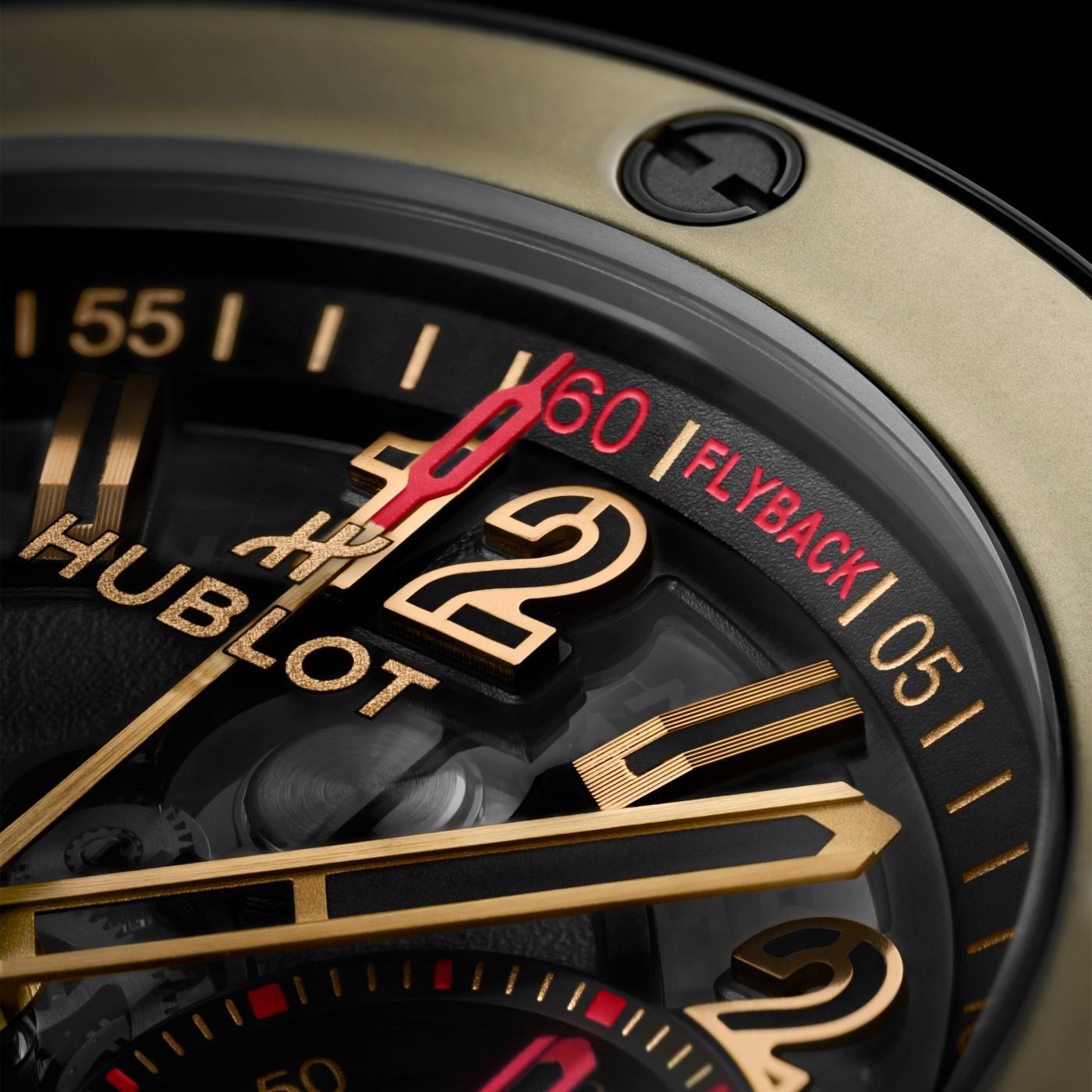 Watch face with gold and black dial, gold hands, red chronograph hand, and "60 FLYBACK" indicator on black bezel.