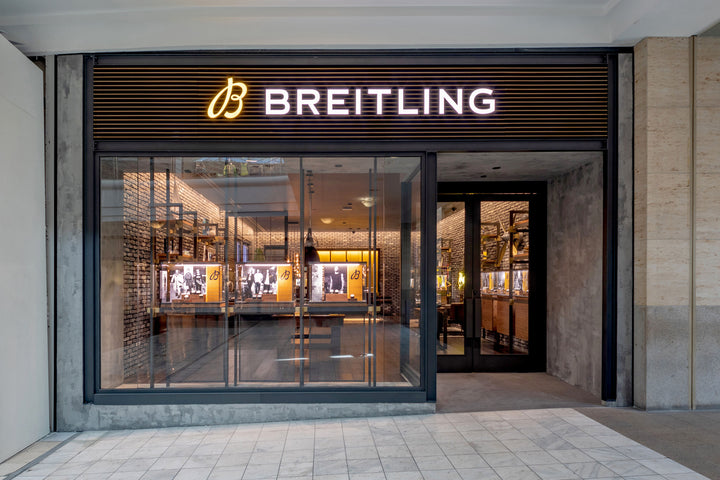 A modern Breitling store exterior with large glass windows and illuminated signage above the entrance.