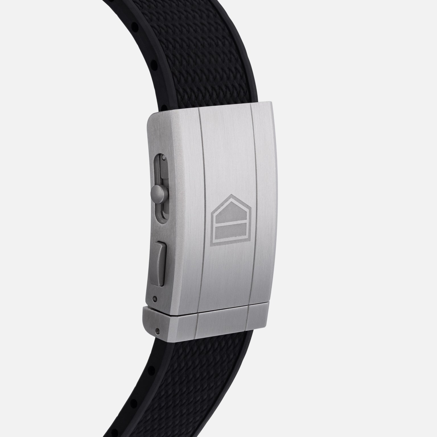 A close-up of the TAG Heuer Carrera Chronograph Seafarer × Hodinkees silver clasp featuring a geometric logo and black textured band.