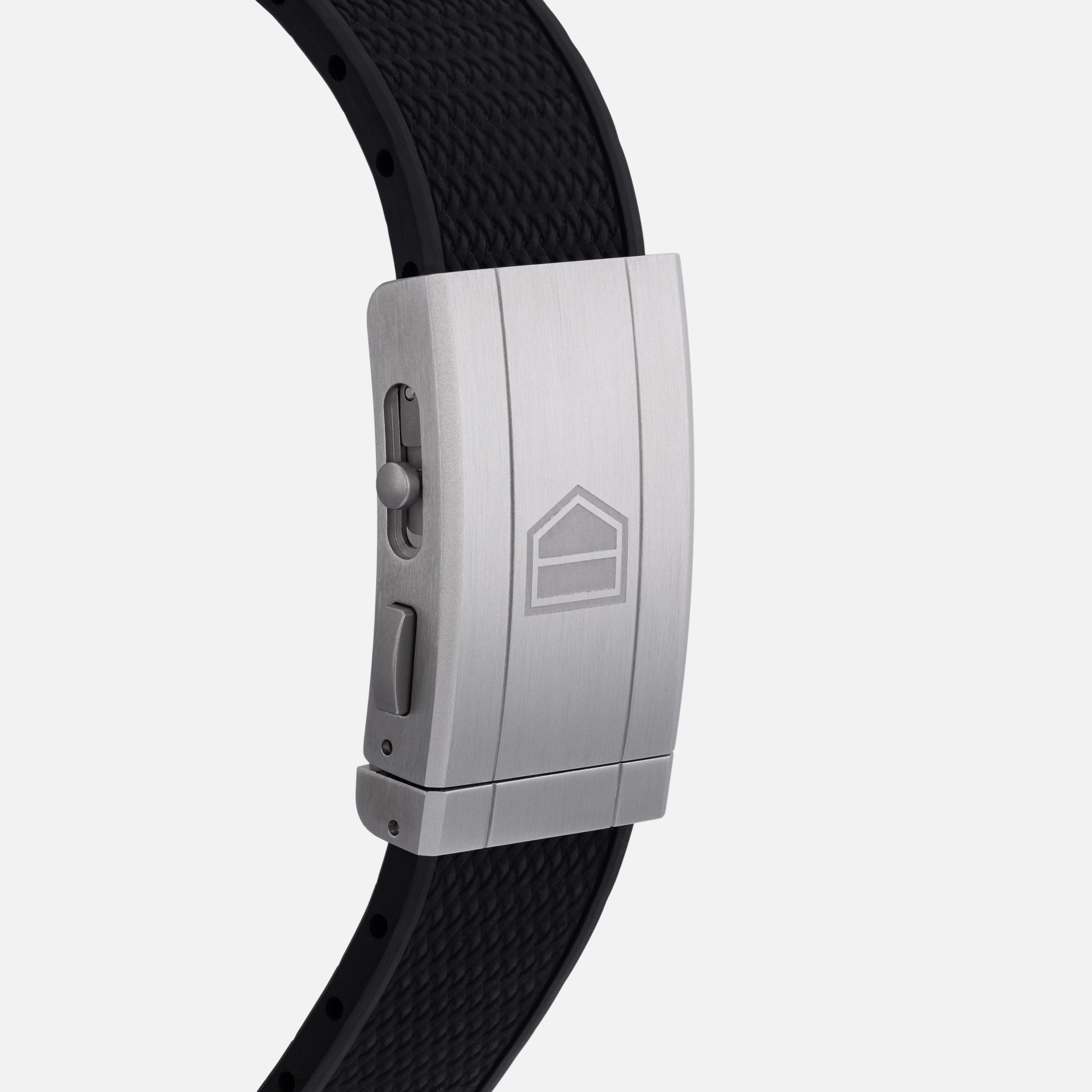 A close-up of the TAG Heuer Carrera Chronograph Seafarer × Hodinkees silver clasp featuring a geometric logo and black textured band.