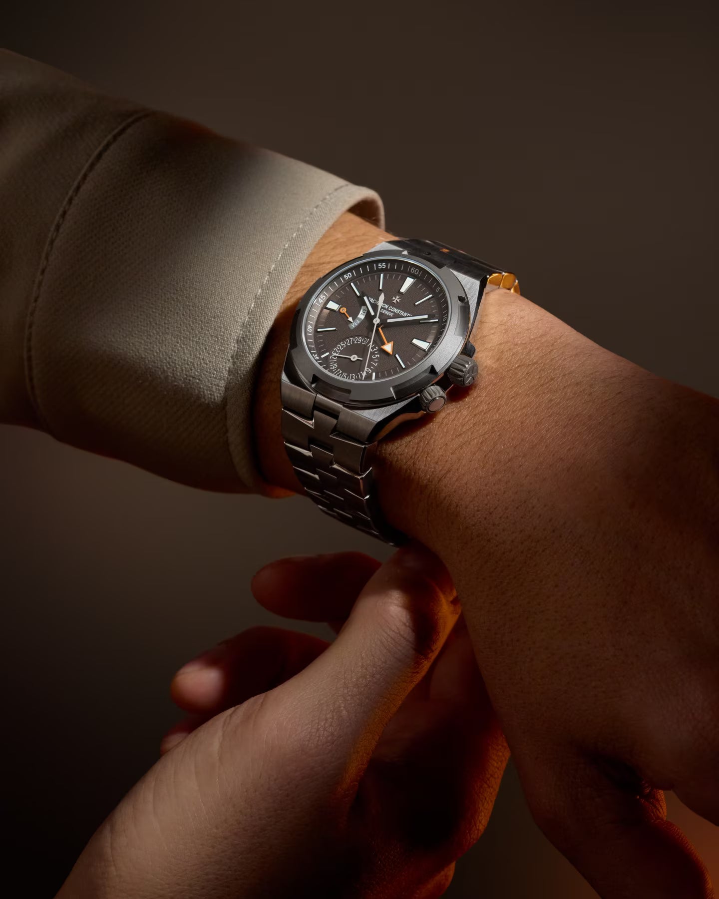 Stainless steel watch with dark dial worn on wrist, featuring dual time zone display and cardinal point markers.