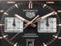TAG Heuer Monaco chronograph watch face with black dial, rose gold hands, two square subdials, and tachymeter bezel.