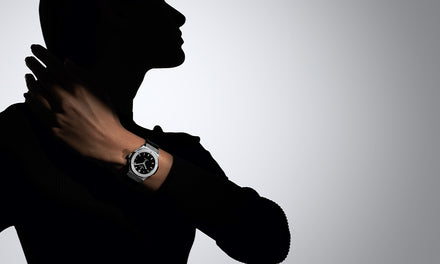 Silhouette of a person posing with a silver wristwatch on their left wrist against a light background.