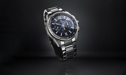 A luxury stainless steel wristwatch with a black and blue dial on a dark gradient background.