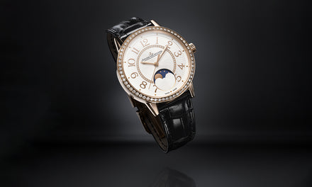 A luxury wristwatch with a black leather strap, gold case, diamond bezel, and moonphase display on the dial.