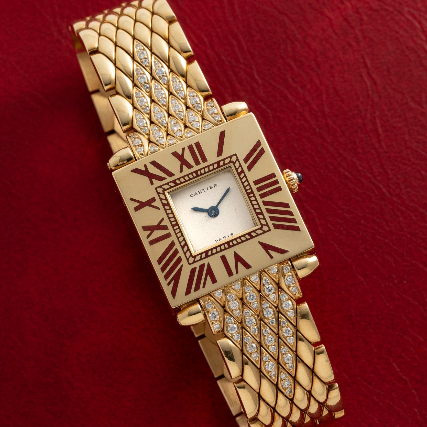 Gold-tone Cartier Obus watch with square dial, Roman numerals, crystal-set bracelet on red background.