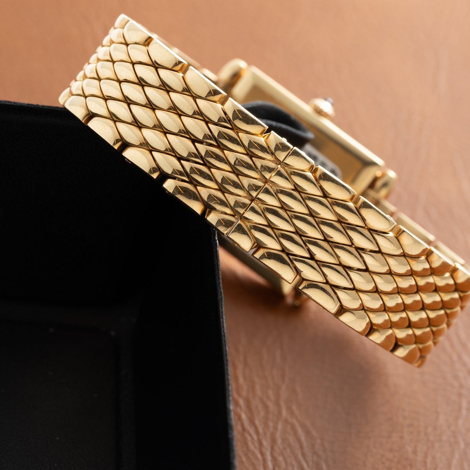 Gold-tone bracelet with quilted scale pattern and polished cylindrical links on tan background.