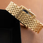 Gold-tone bracelet with quilted scale pattern and polished cylindrical links on tan background.