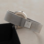 Piaget’s Lapis Lazuli Dress Watch with a silver mesh band and square clasp rests on a light surface beside its black box.