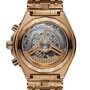 Gold-tone chronograph watch with visible mechanical movement through transparent case back and matching bracelet.