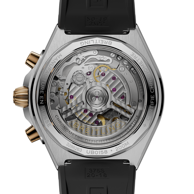 Stainless steel watch with exposed mechanical movement, gold-tone chronograph pushers, and black rubber strap.