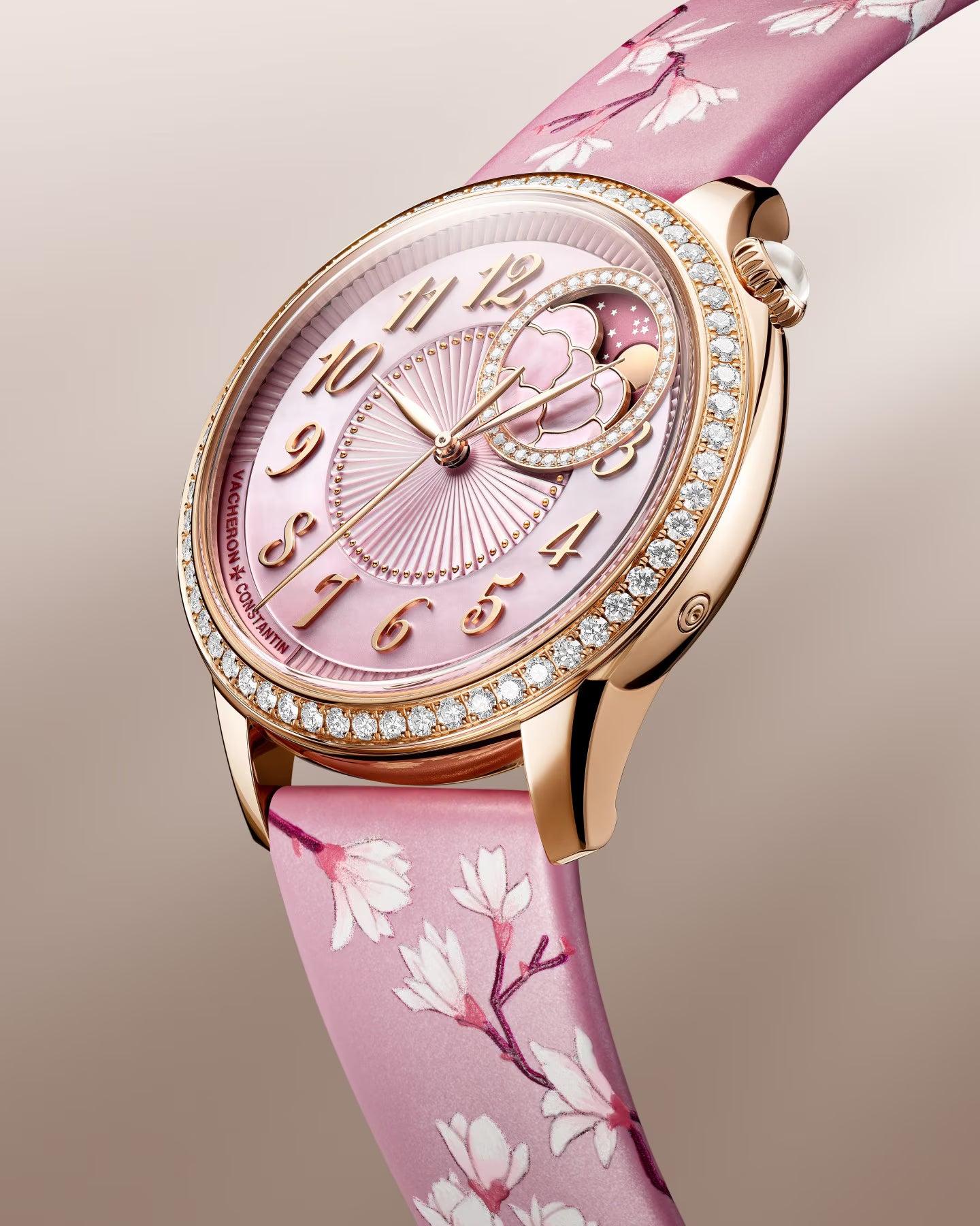 Rose gold watch with pink mother-of-pearl dial, crystal-set bezel, moon phase subdial, and pink silk strap with floral patter