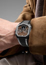 Luxury watch on a person's wrist with a brown jacket