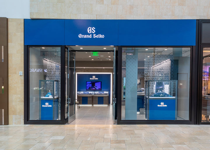 Grand Seiko store with blue signage, glass doors, and watch displays inside a shopping mall.