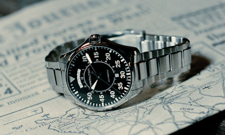 A Hamilton watch with a silver strap and black dial sitting on a newspaper with a black and white vintage-appearing map