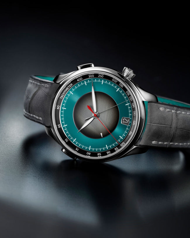 Silver chronograph watch with teal dial, black leather strap, and dual time zone subdial.