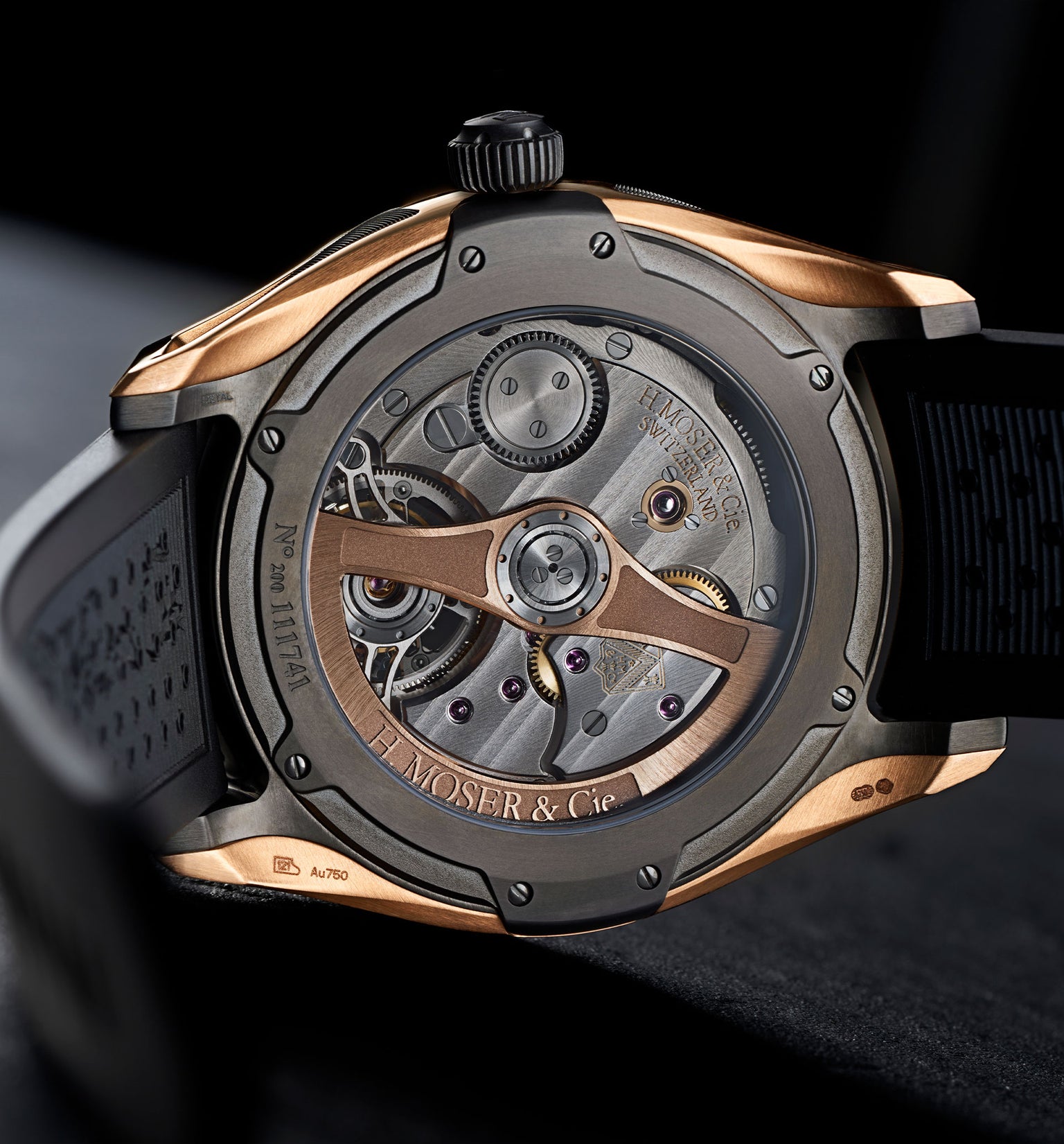 Tourbillon watch with rose gold and gunmetal case, visible mechanical movement and exposed balance wheel, black rubber strap.