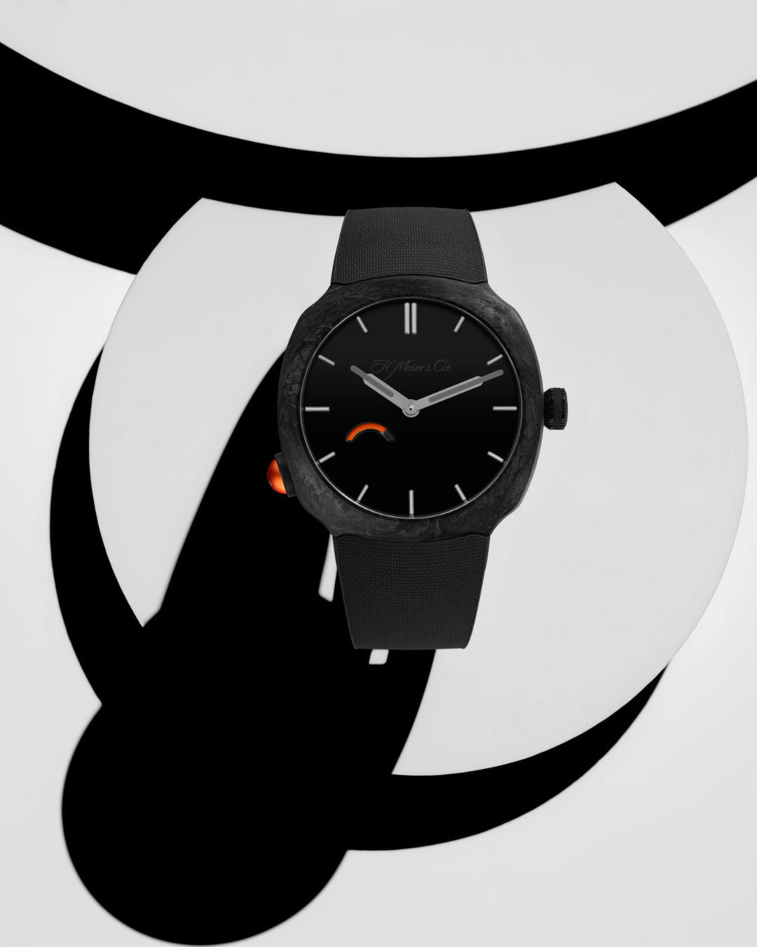 Black watch with minimalist dial, silver hands, orange accent detail on side, and black textile strap.