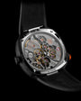 Luxury watch with visible mechanical movement, gold and silver gears, red crown, black rubber strap, and stainless steel case