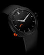 Black watch with textured case, silver hands and hour markers, orange accent details, and black textile strap.