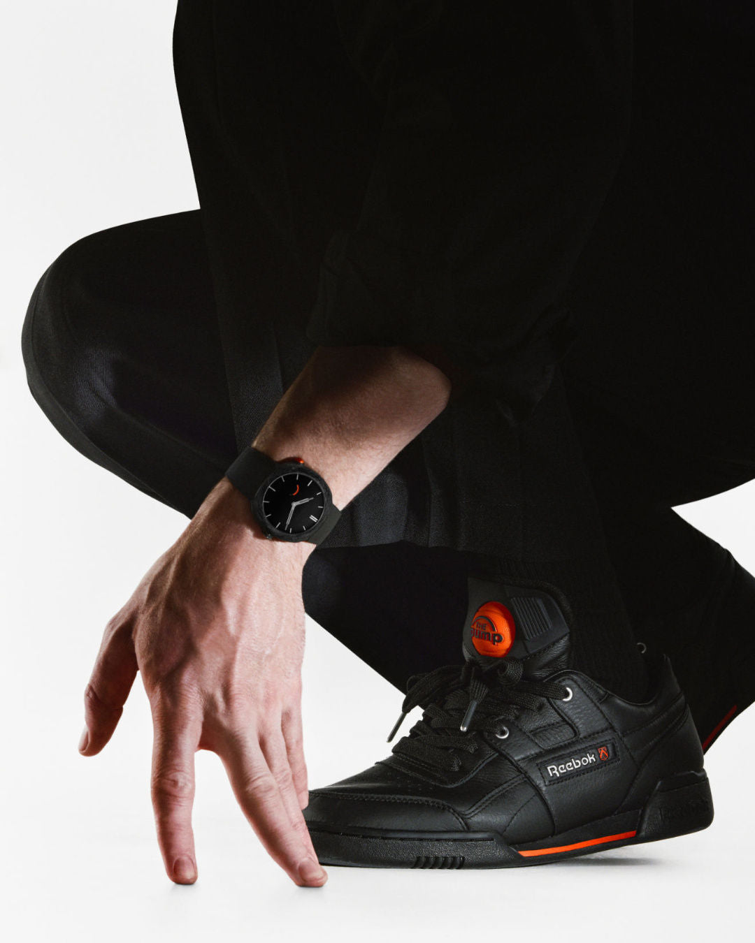 Black and orange Reebok high-top sneaker with lace-up closure displayed on a person's foot.