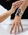 Two wristwatches with white metal bracelets worn on one wrist, featuring black and burgundy dial faces with minimalist design