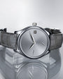 Tantalum watch with silver dial, minimalist hour markers, and dark leather strap displayed against reflective surface.