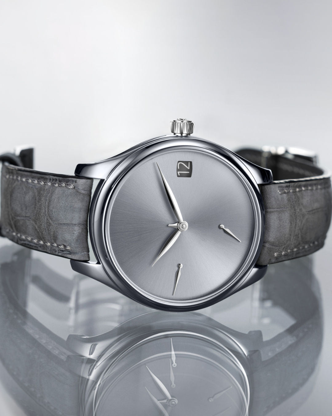Tantalum watch with silver dial, minimalist hour markers, and dark leather strap displayed against reflective surface.