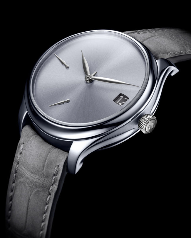 Tantalum watch with brushed silver dial, three hands, date window, and gray leather strap against black background.