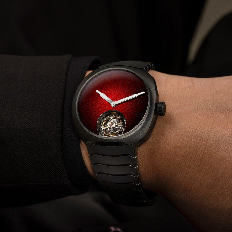 Black watch with red face on a wrist against a dark background