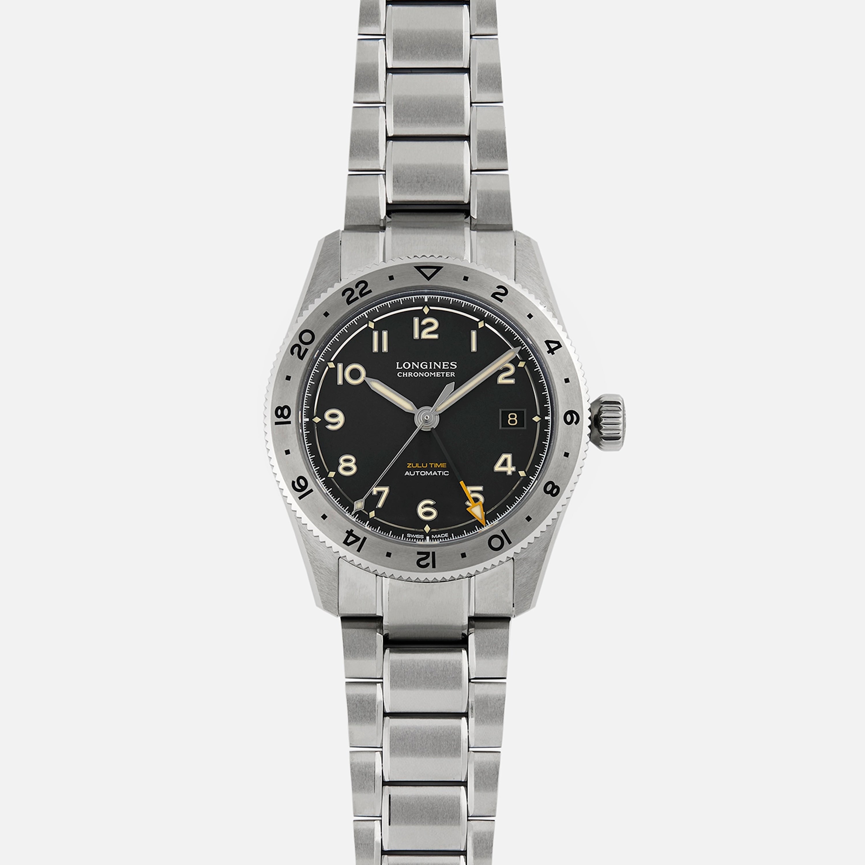 The Longines Spirit Zulu Time Limited Edition For Hodinkee features a black dial with Arabic numerals, date at 3 o’clock, and a metal bracelet. Crafted from Grade 5 Titanium by Longines, it is shown on a plain white background.