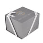 A gray gift box with white ribbon, featuring Watches of Switzerland Group branding and a gold circular lid design inspired by the iconic OMEGA Seamaster Aqua Terra 150M and its exceptional 8800 calibre movement.