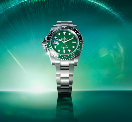 Rolex GMT-Master II watch with a green dial and a silver toned bracelet centered over a glowing green background 