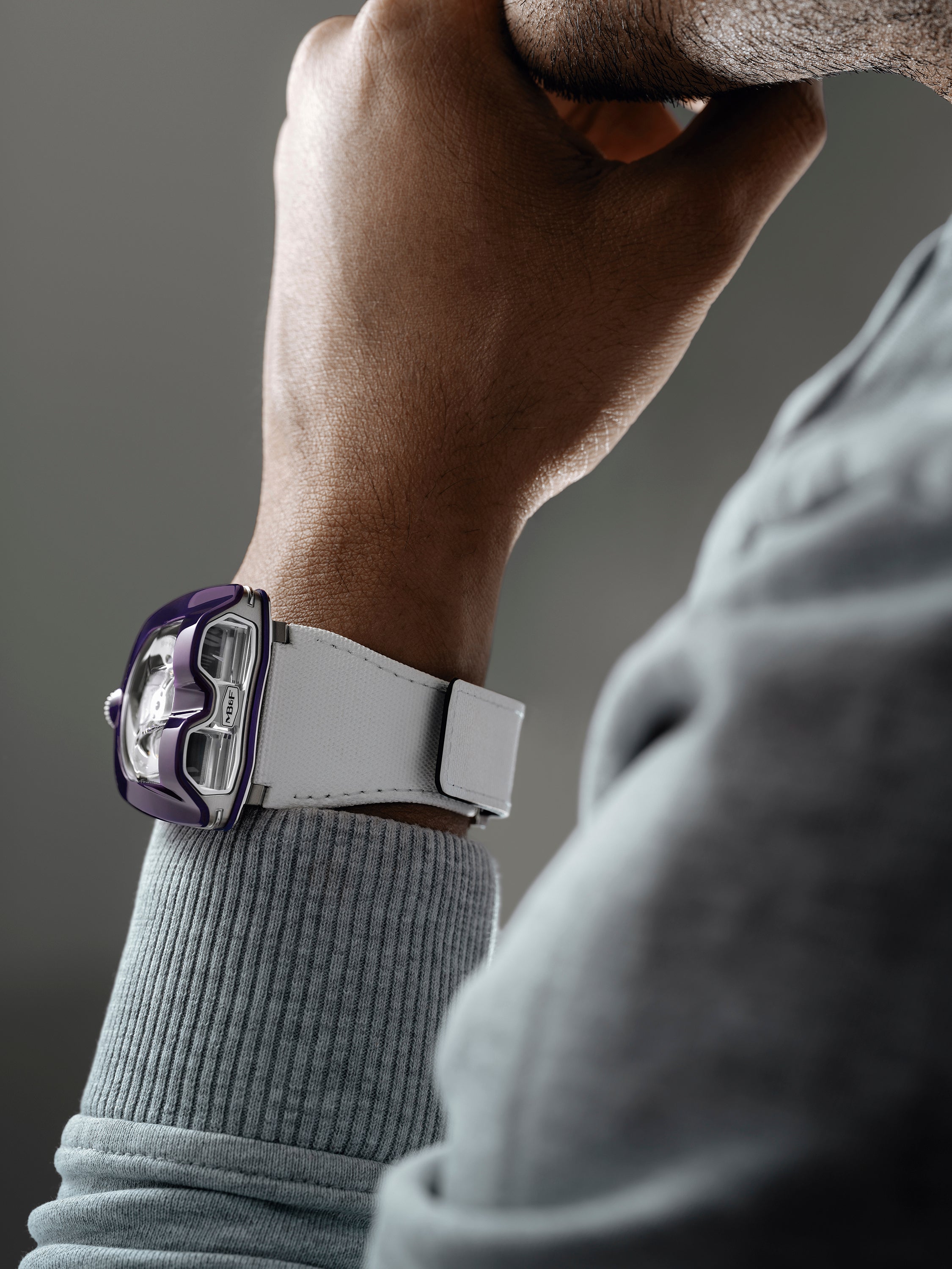 Close-up of a person wearing the MB&F HM8 Mark 2 Titanium Limited Edition Watch in white and purple, resting their hand on their chin.