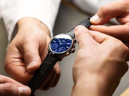 Four hands hold the black leather strap of a watch with a blue dial and Czapek text logo