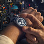 Close-up of a person's wrist wearing a watch with an aircraft cockpit in the background