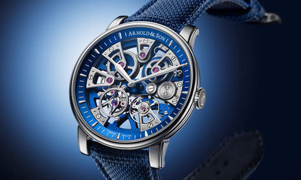 A luxury skeleton watch with visible gears, blue accents, and a blue textured strap against a gradient background.