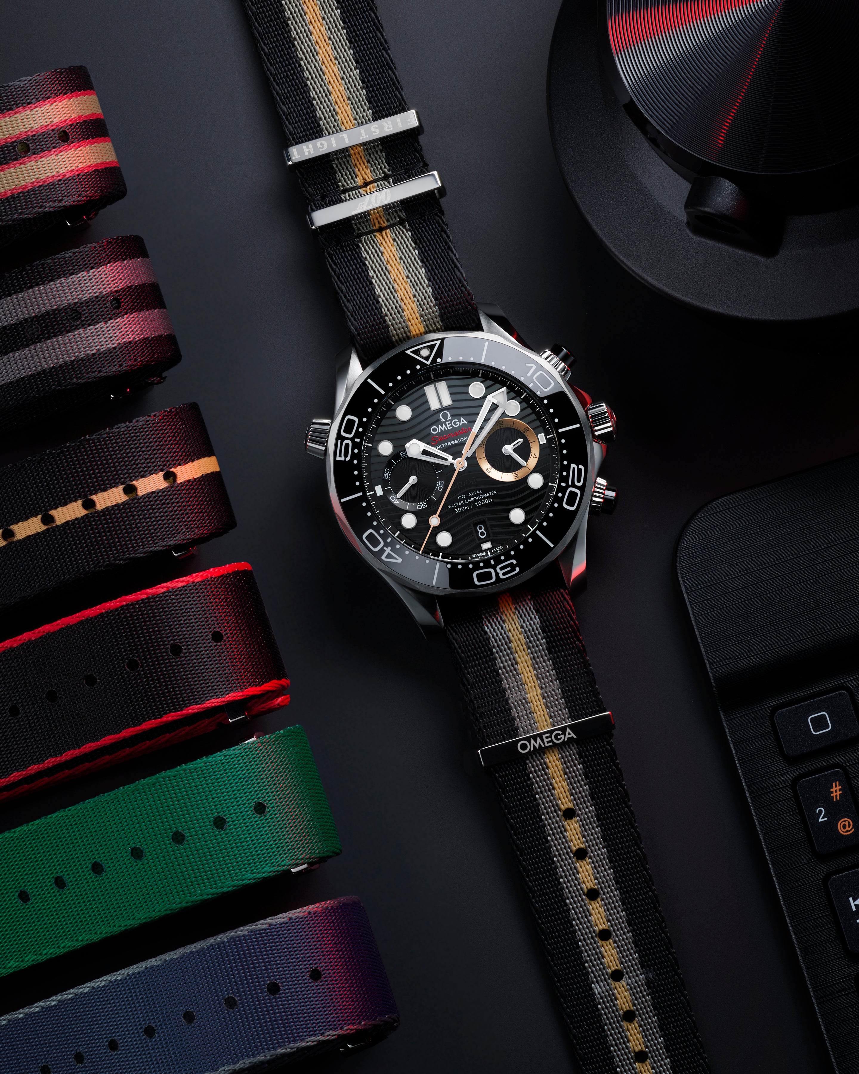 Stainless steel chronograph watch with black dial, white hour markers, and striped fabric strap with red and gold accents.